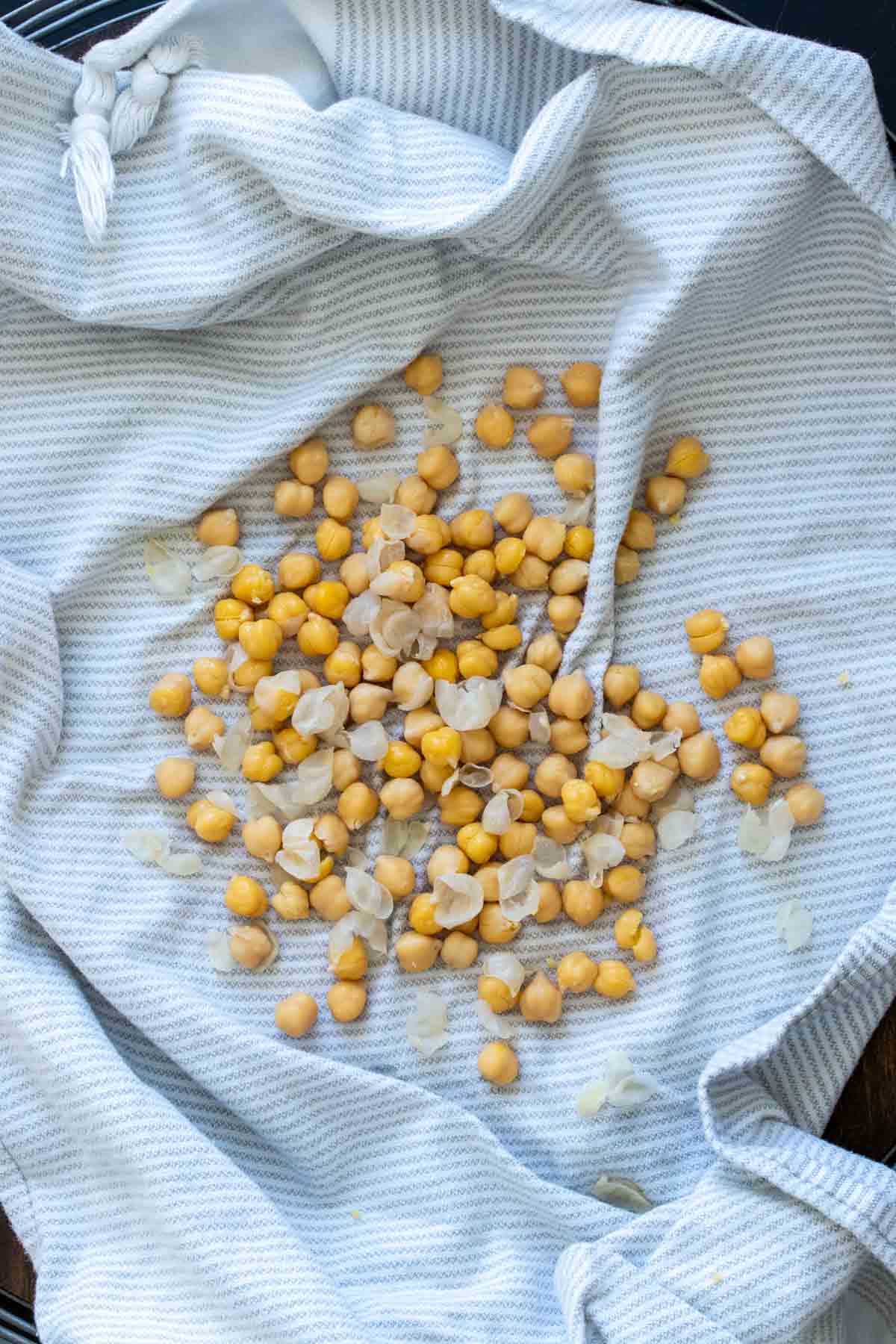 Cooked chickpeas with skins half off on a white kitchen towel.