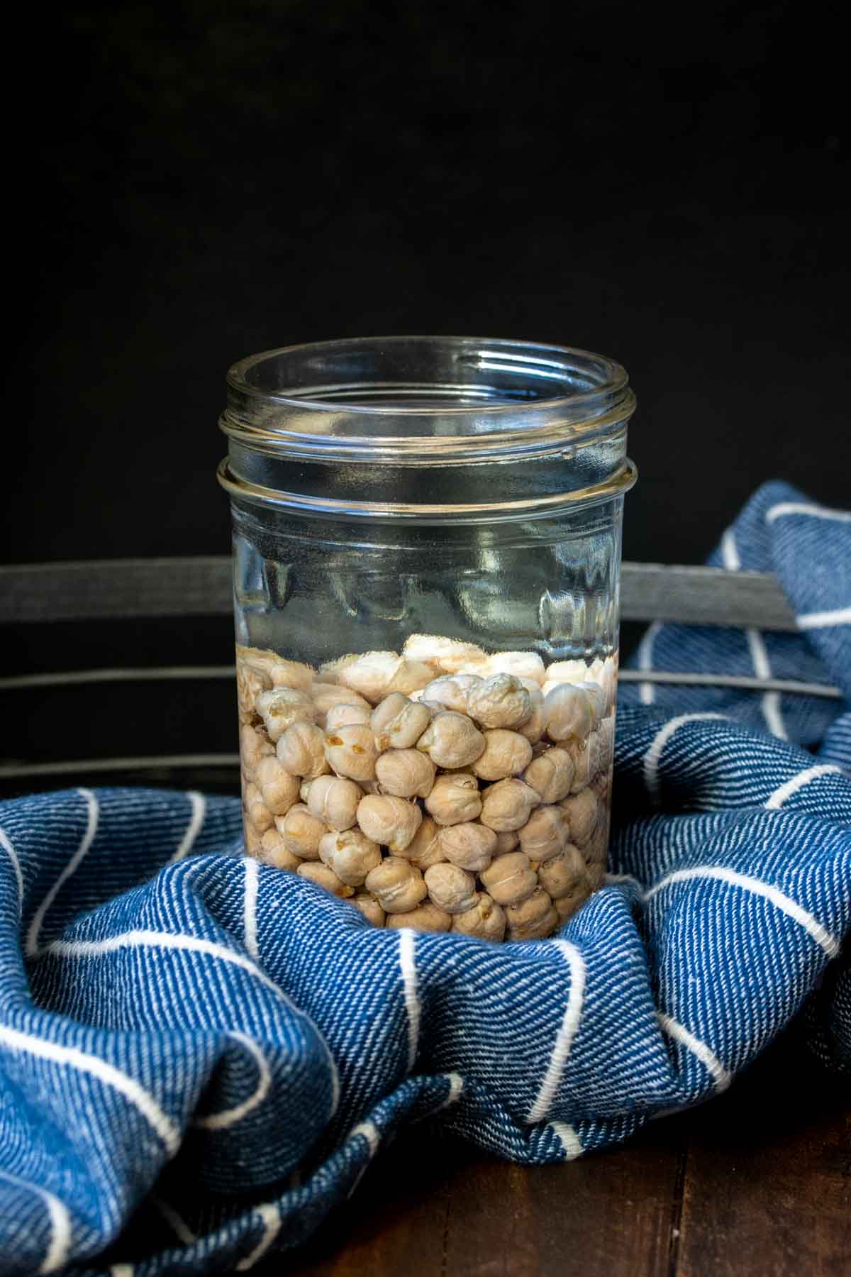 Glass jar filled with water and dried chickpeas filled up halfway inside.