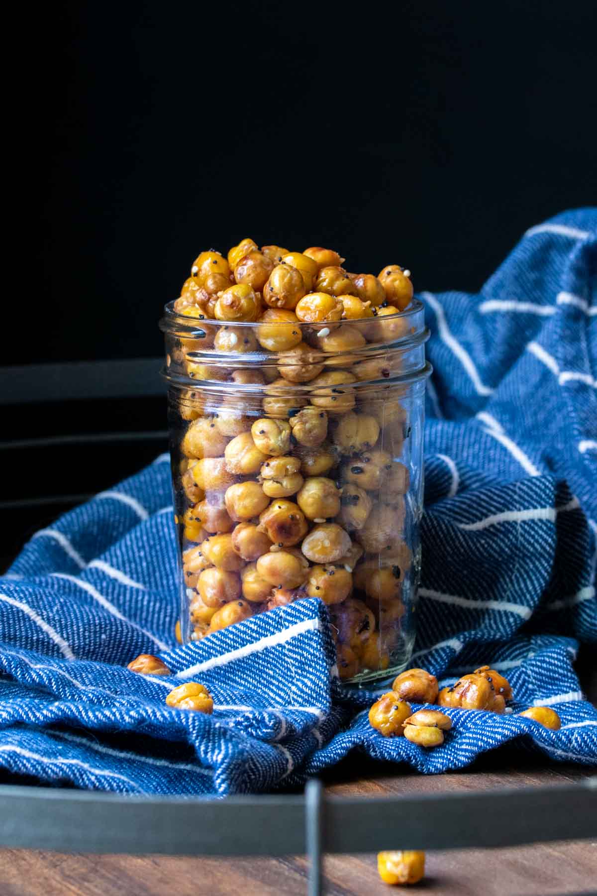 Glass jar on a blue striped towel filled with roasted crispy chickpeas.