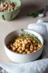 A white bowl with tan trim and cooked chickpeas with thyme inside.