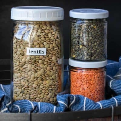 Glass jars filled with different colors of dry lentils on a wooden tray
