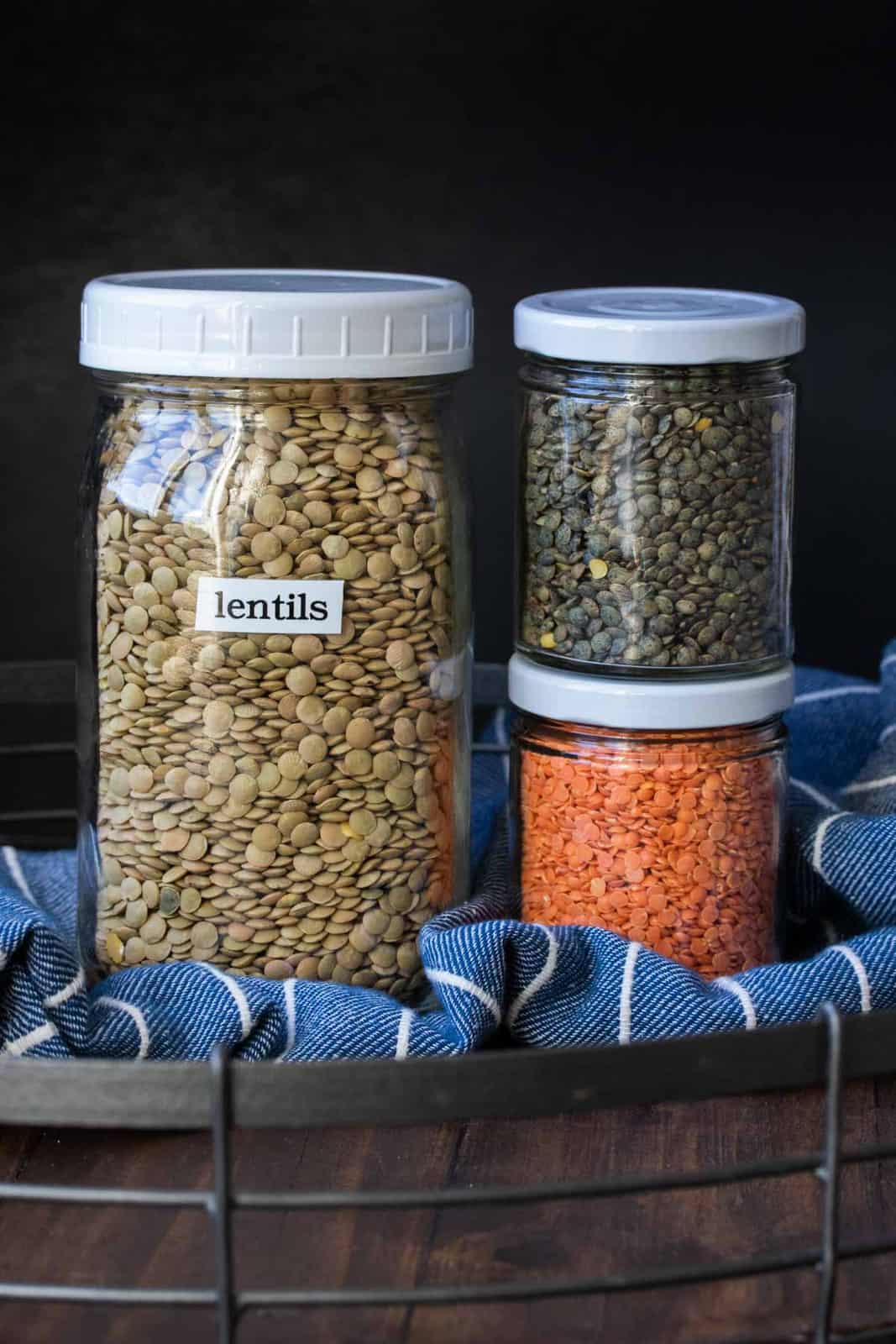 Glass jars filled with different colors of dry lentils on a wooden tray