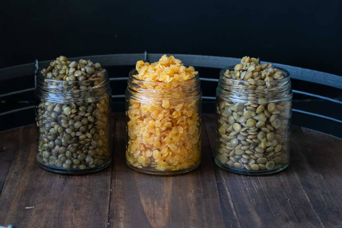 Three glass jars on a wooden tray filled with different colored cooked lentils