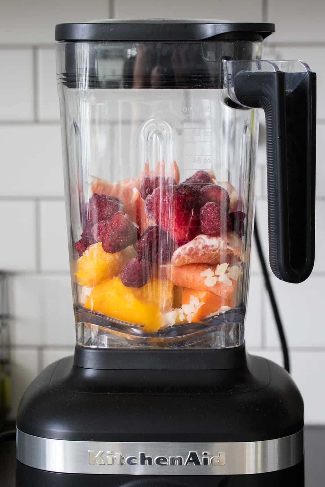 Blender filled with oranges, mango and berries