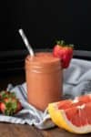 Glass jar with a salmon colored smoothie and a strawberry on the side