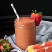 Glass jar with a salmon colored smoothie and a strawberry on the side