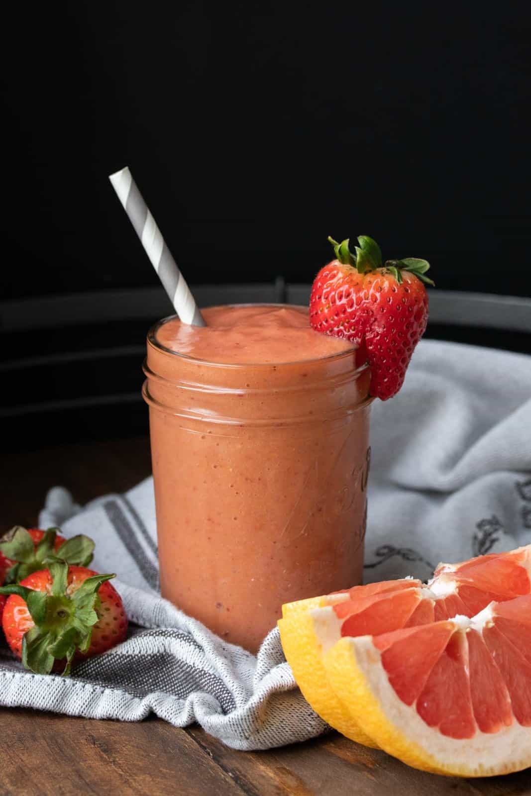 Glass jar with a salmon colored smoothie and a strawberry on the side