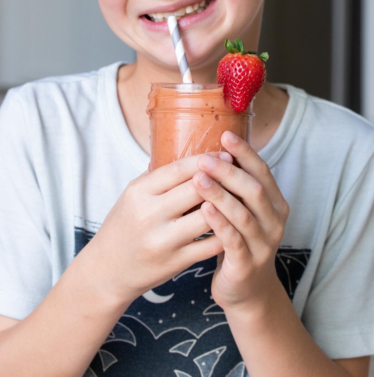 Boy drinking a salmon colored smoothie from a grey striped straw