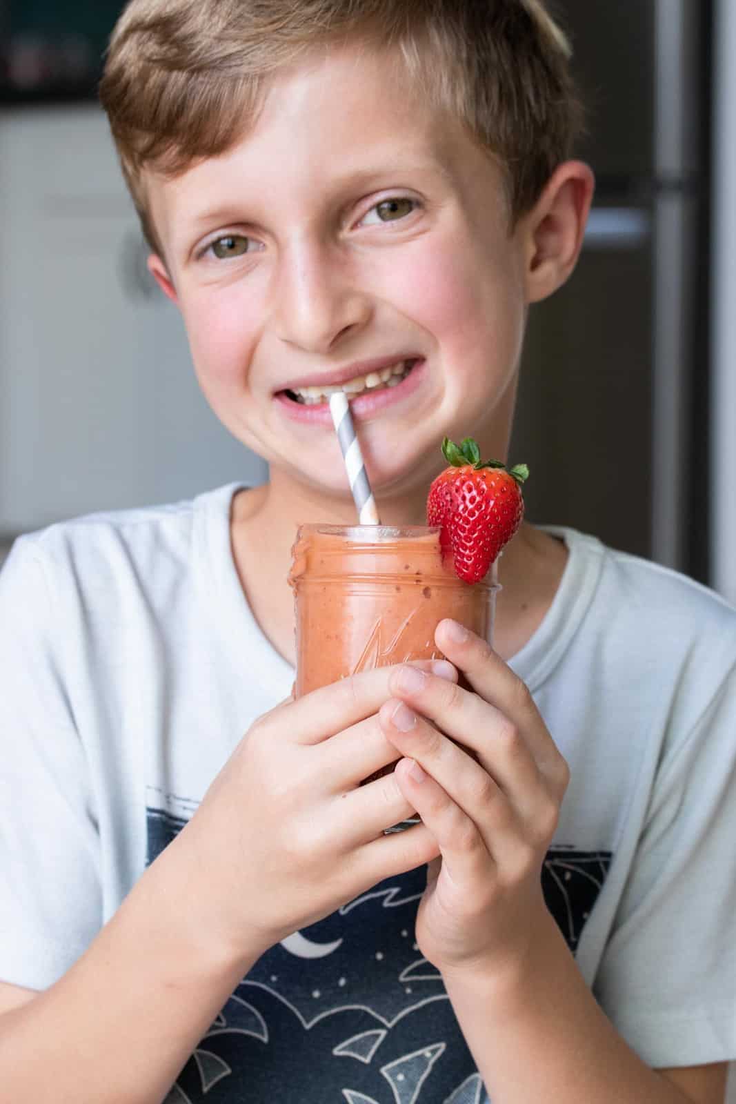 Boy drinking a salmon colored smoothie from a grey striped straw