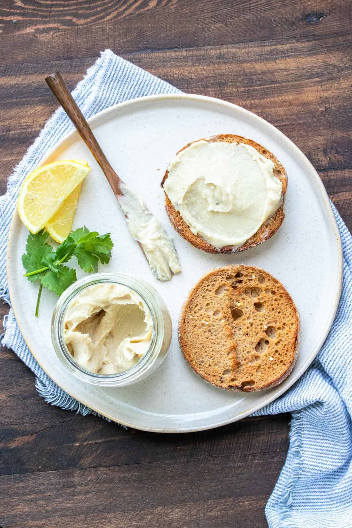 English muffin in two halves one with with plain cream cheese on a white plate