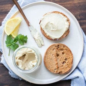 White plate with an english muffin spread with cream cheese on top.