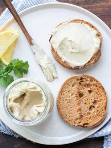 White plate with an english muffin spread with cream cheese on top.