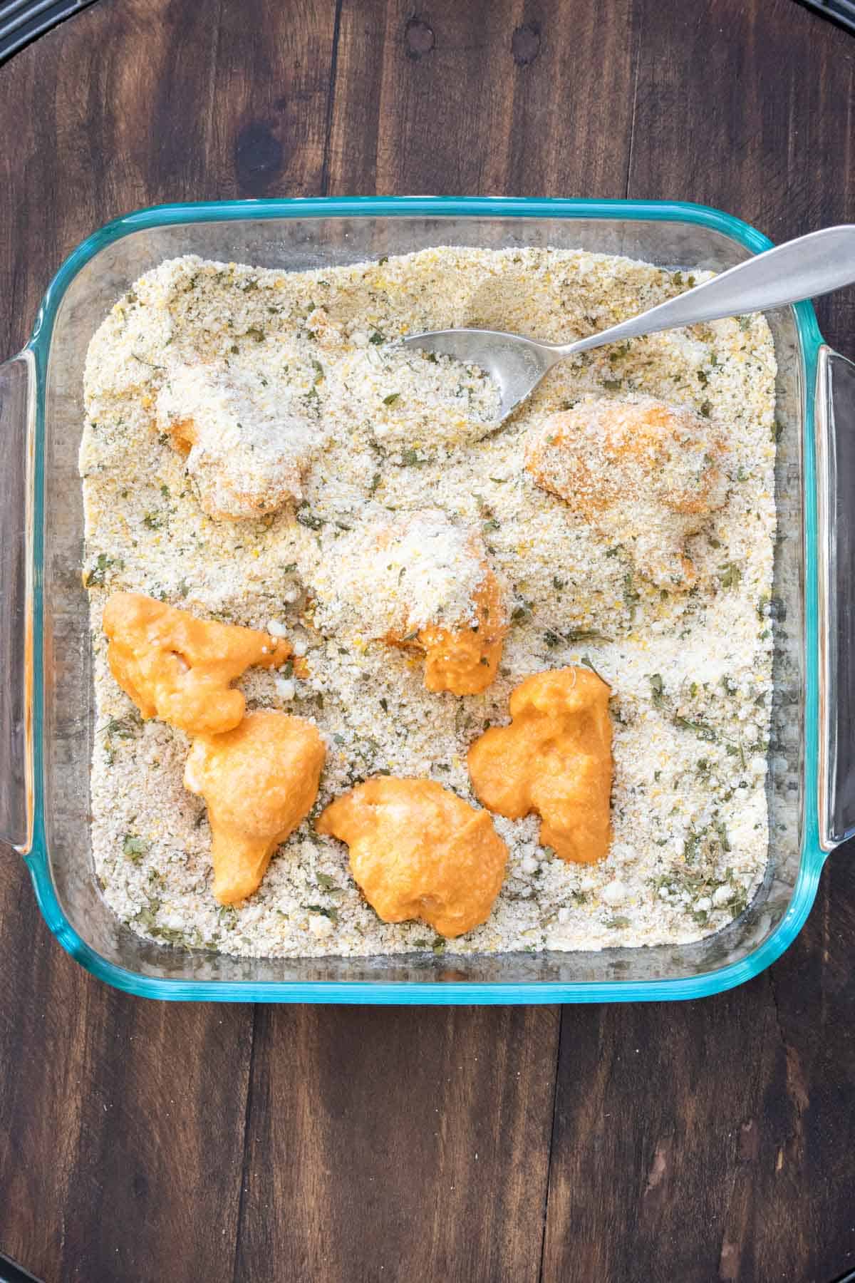 Cauliflower pieces dipped in orange batter being coated with a breadcrumb mixture.