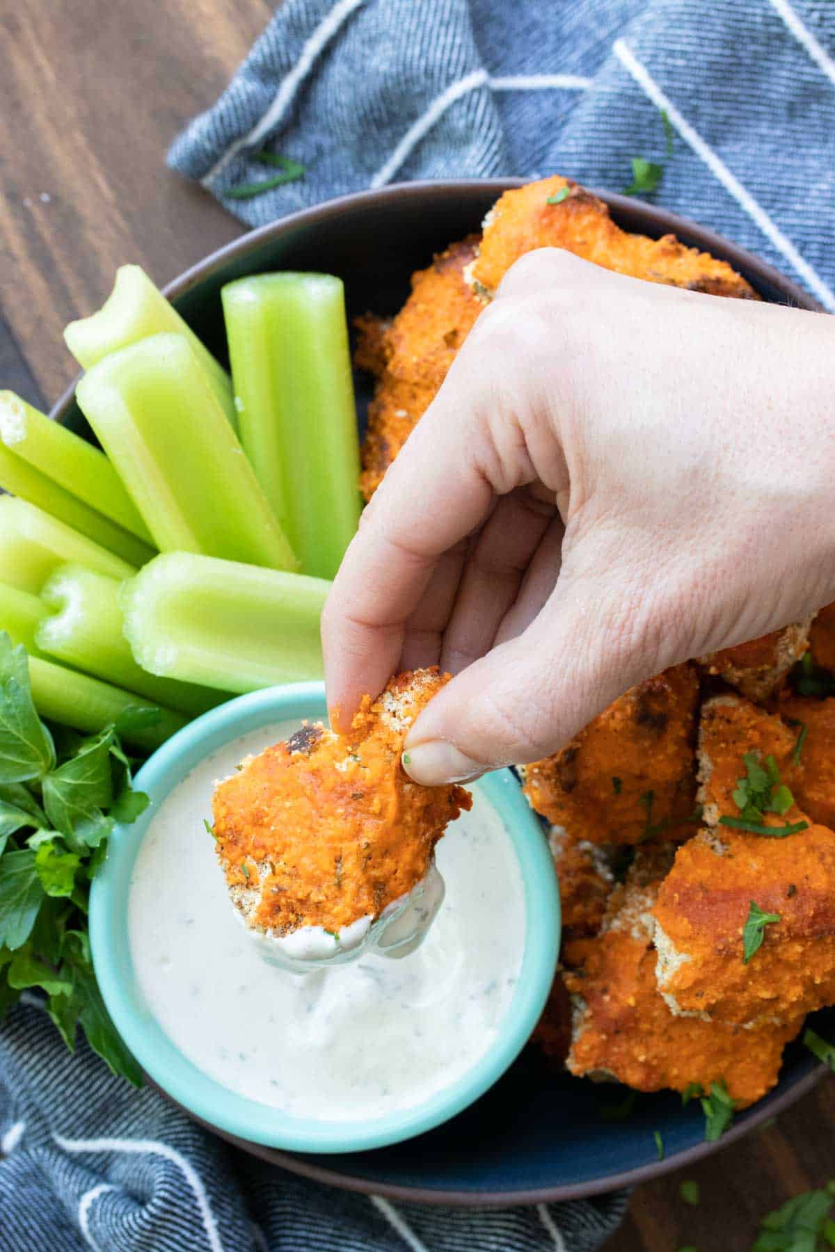 Hand dipping a buffalo cauliflower wing into a bowl of ranch dip.