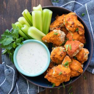 A black bowl with ranch, celery pieces and buffalo cauliflower wings.