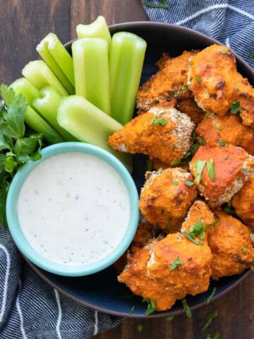 A black bowl with ranch, celery pieces and buffalo cauliflower wings.