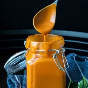 A glass jar with buffalo sauce in it and dripping from the top of the jar.