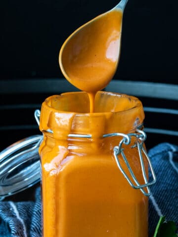 A glass jar with buffalo sauce in it and dripping from the top of the jar.