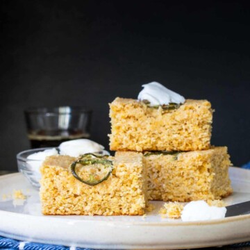 Square pieces of corn bread with jalapeños on top stacked on a cream plate