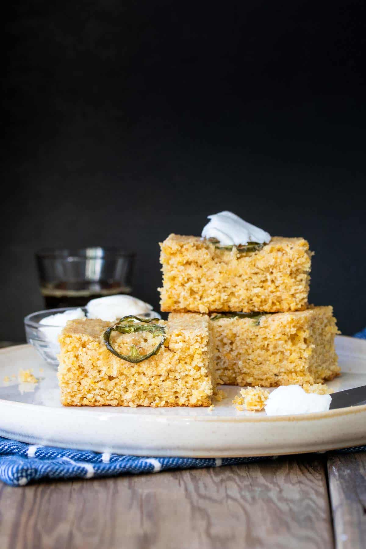 Square pieces of corn bread with jalapeños on top stacked on a cream plate