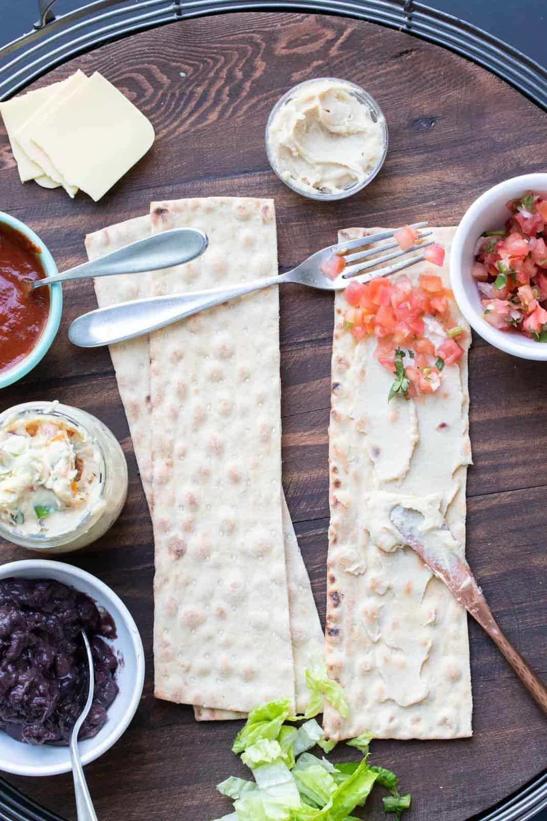 Knife spreading cream cheese and fork spreading salsa on slices of lavash bread