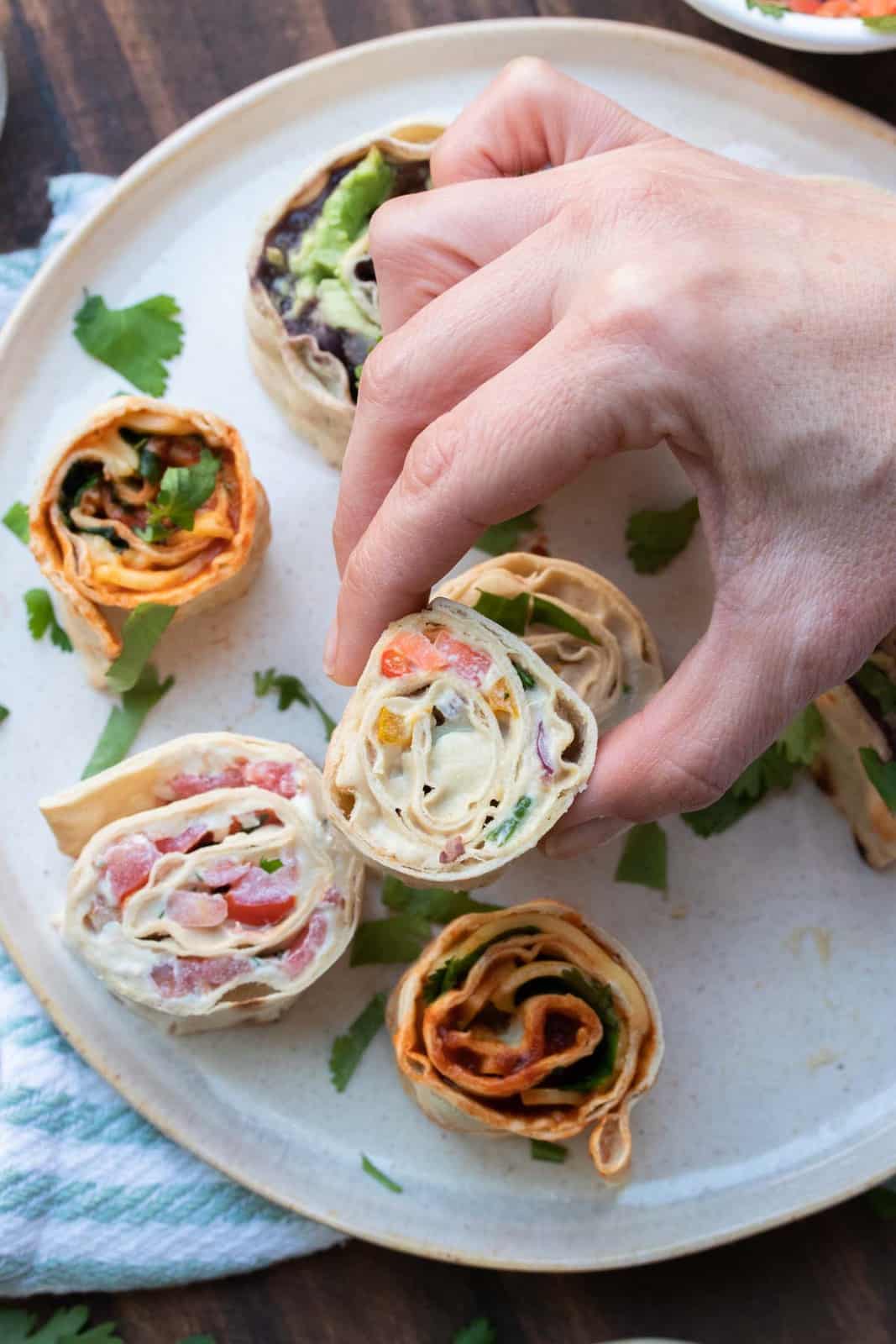 Hand grabbing a pinwheel sandwich filled with veggies and cream cheese