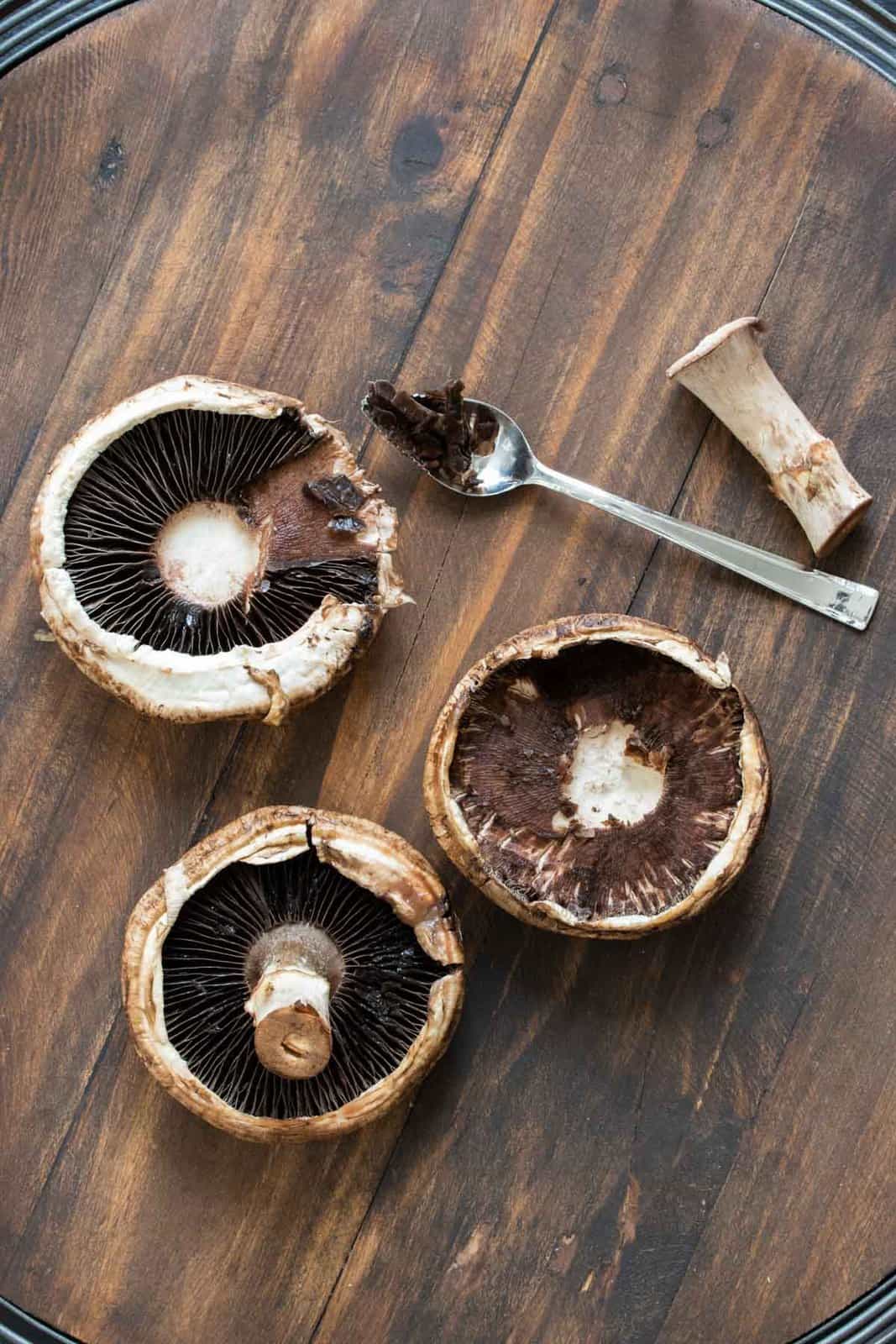 Three portobello mushrooms on a wooden table being cleaned