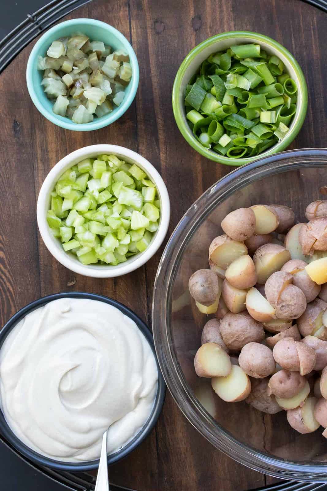 Bowls filled with ingredients for potato salad on a wooden surface