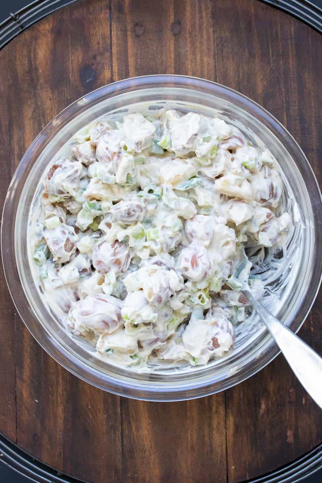 Creamy potato salad in a glass bowl with a spoon in it