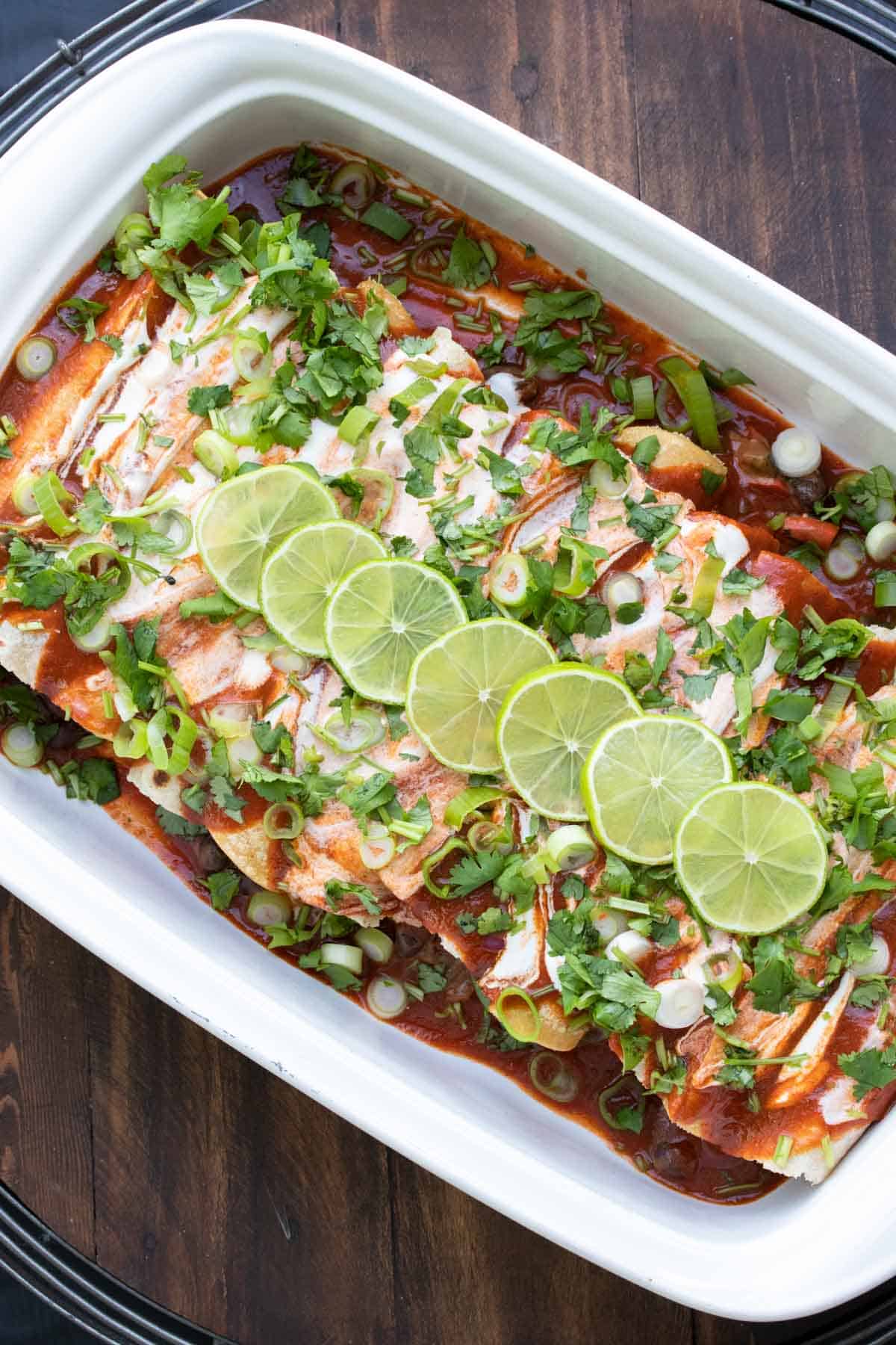 Uncooked enchiladas with red and white sauce, green onions and sliced limes.