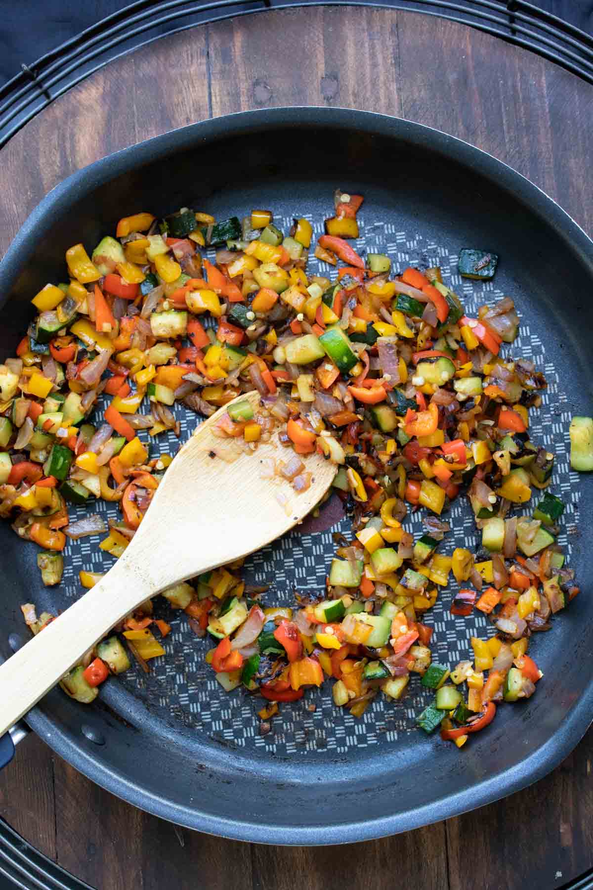 Wooden spoon mixing chopped veggies in a pan.