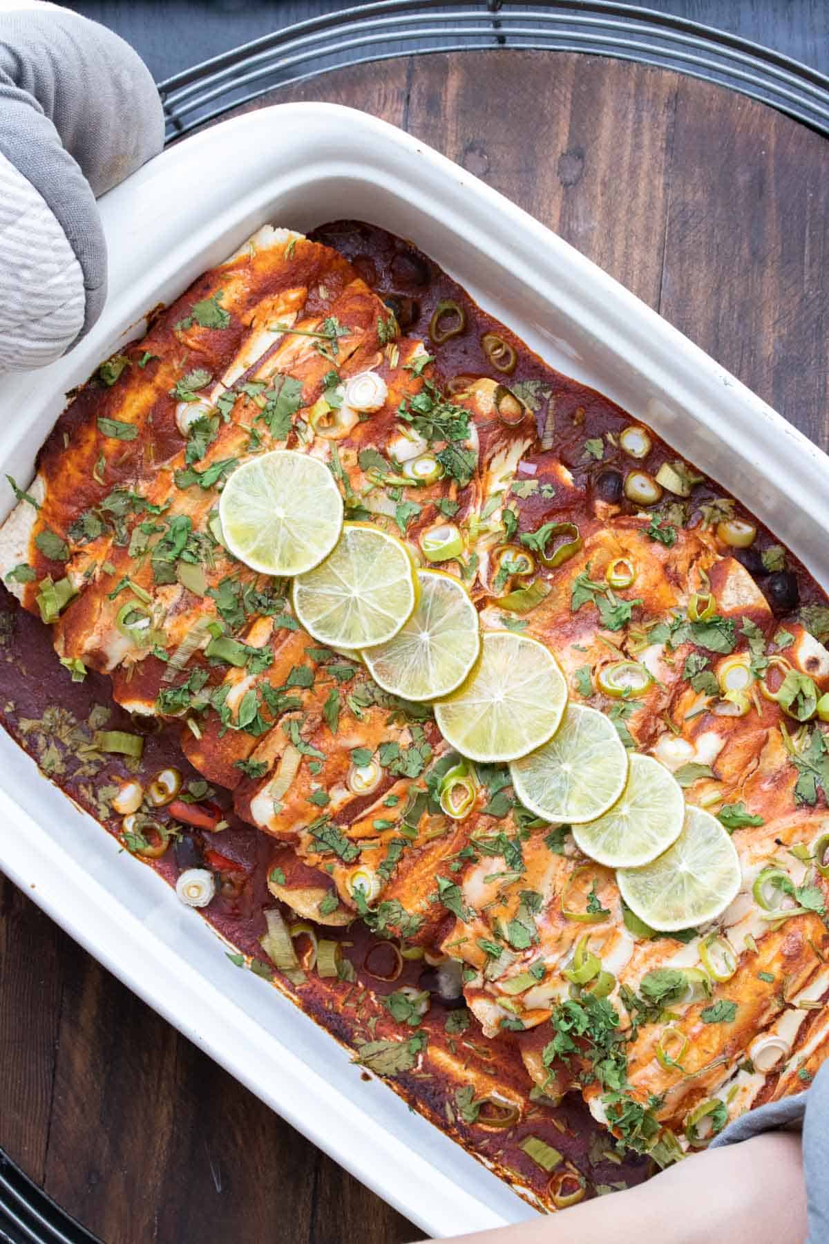 Baked enchiladas with red sauce topped with green onions and limes.