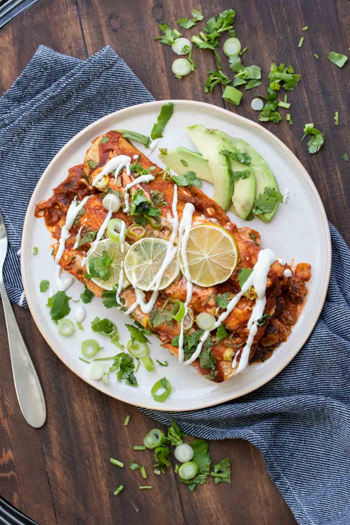 White plate with two red sauce enchiladas drizzled with sour cream