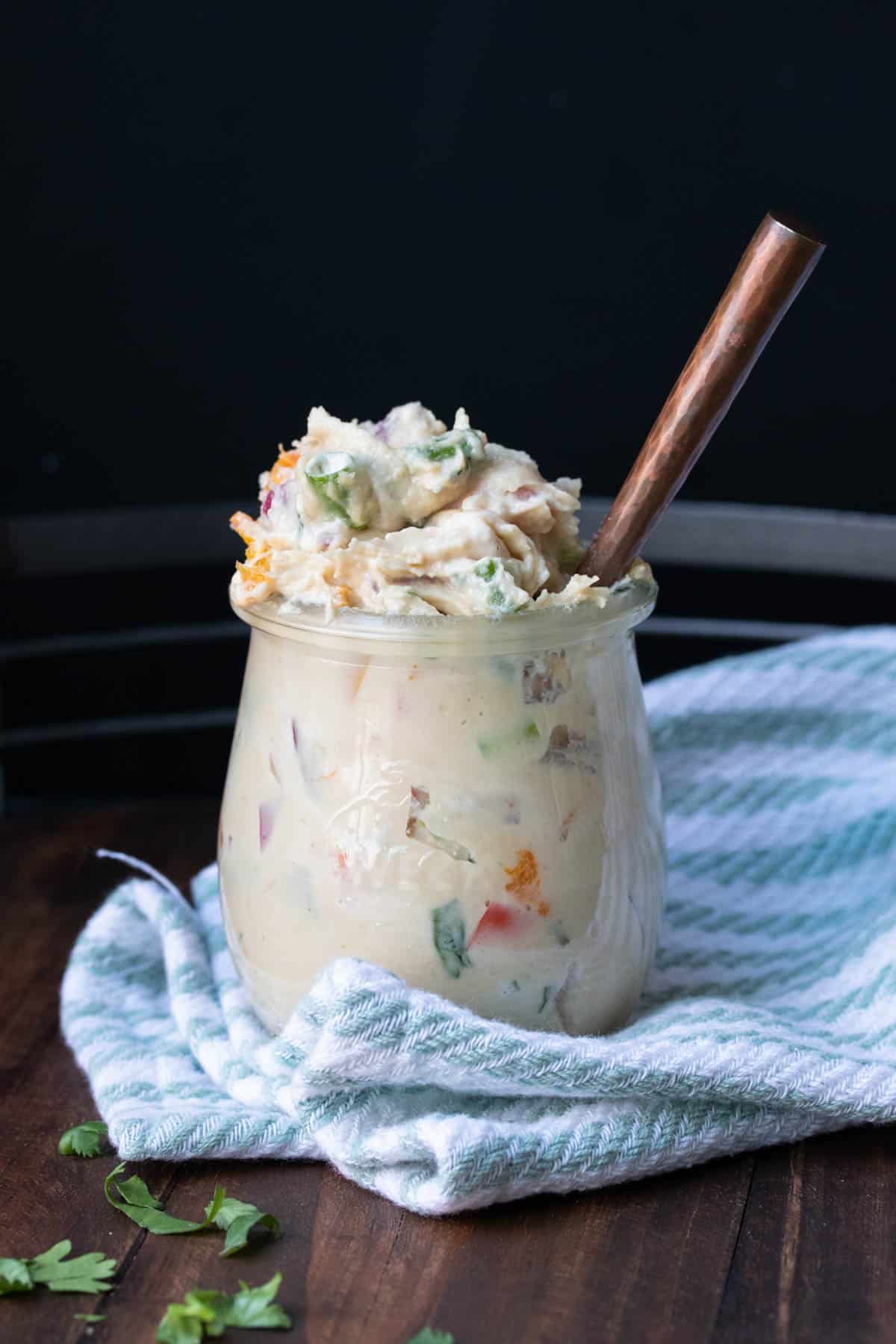 Glass jar filled with veggie cream cheese and a copper spoon in it