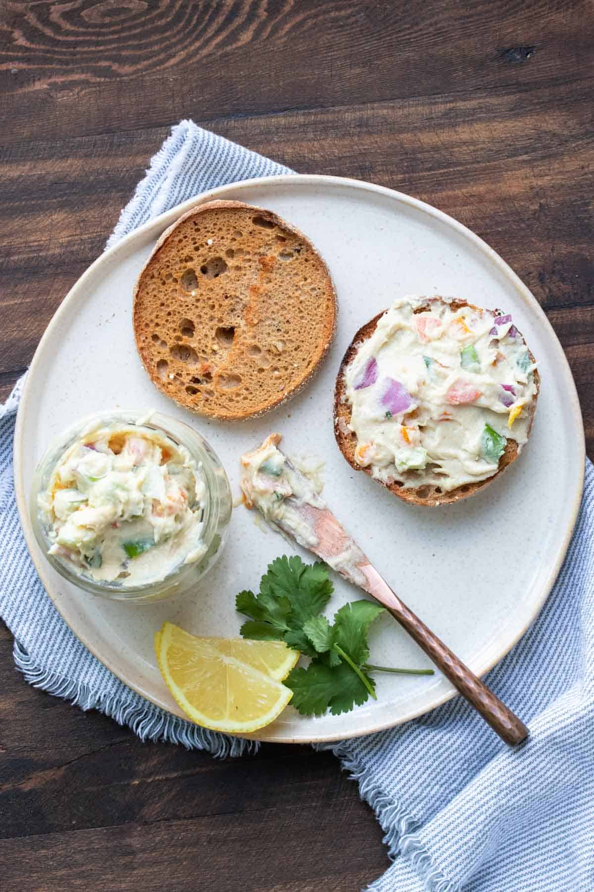 Veggie cream cheese spread on half an english muffin on a white plate