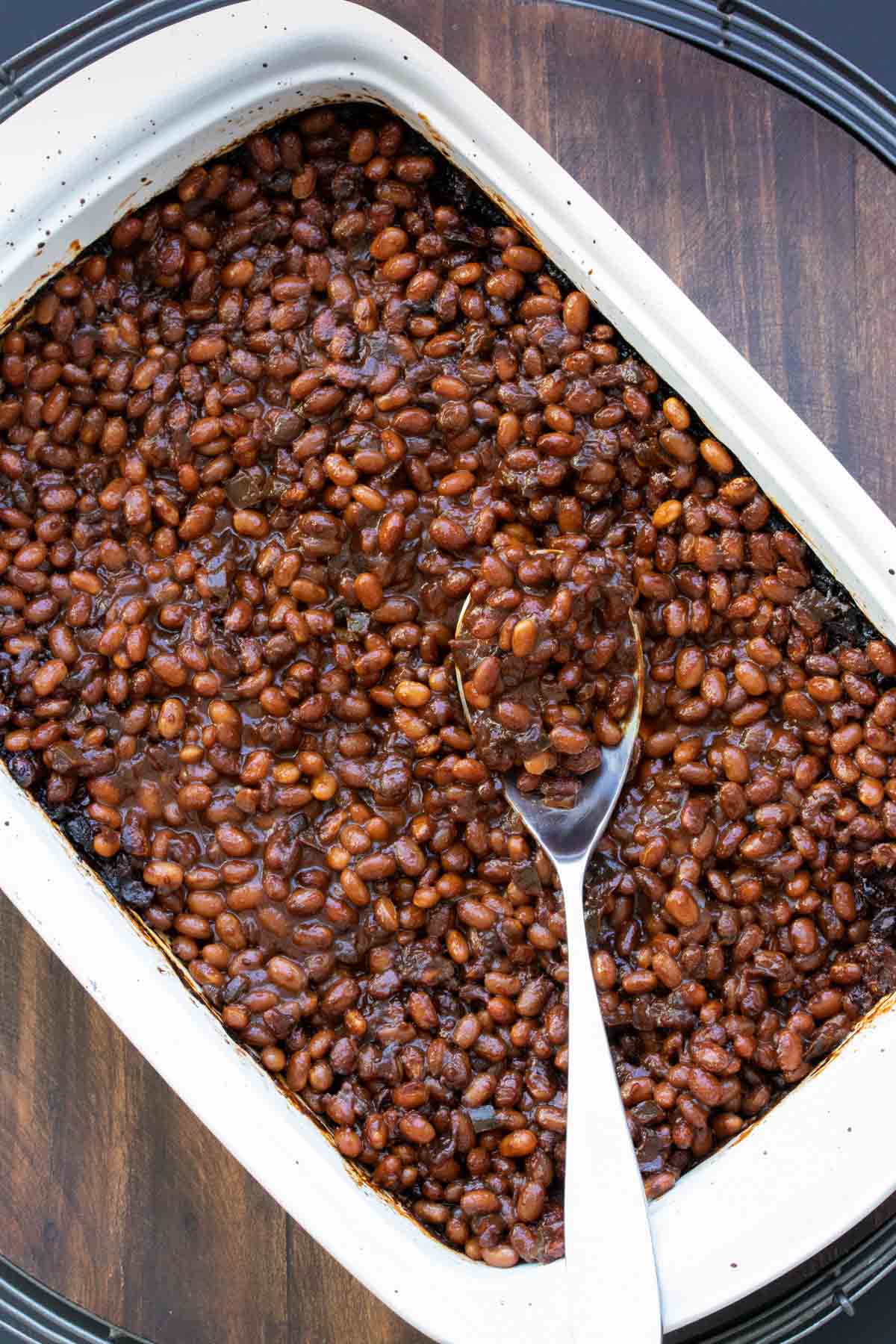 Spoon scooping out baked beans from a white baking dish