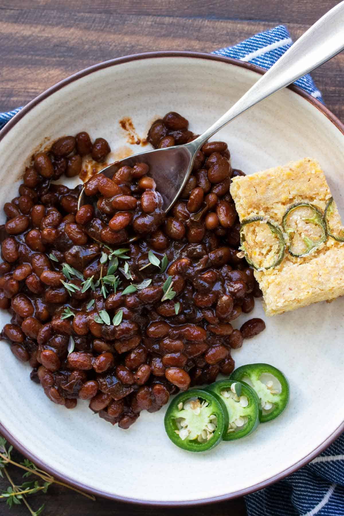 Spoon getting a bite of baked beans from a cream plate