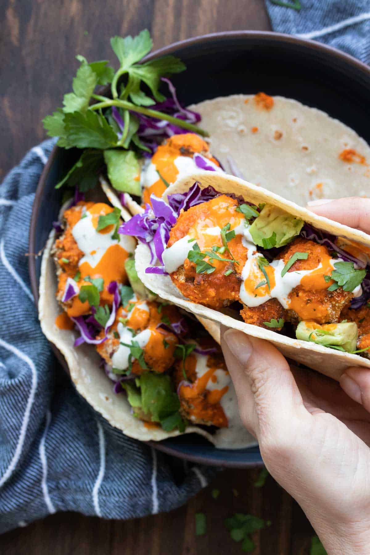 Hand holding a crispy buffalo cauliflower taco with toppings