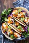 Close up of three buffalo cauliflower tacos topped with cabbage and avocado