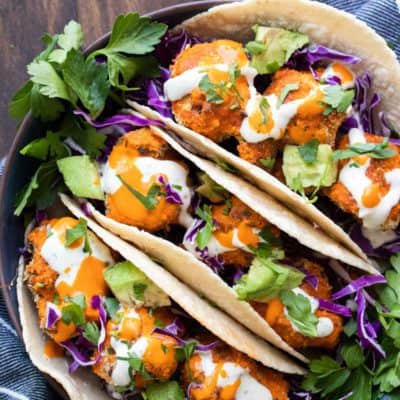 Close up of three buffalo cauliflower tacos topped with cabbage and avocado