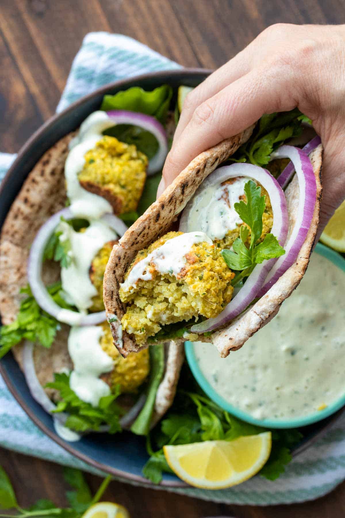 Hand holding a half eaten falafel pita sandwich with onion and tzatziki on top.