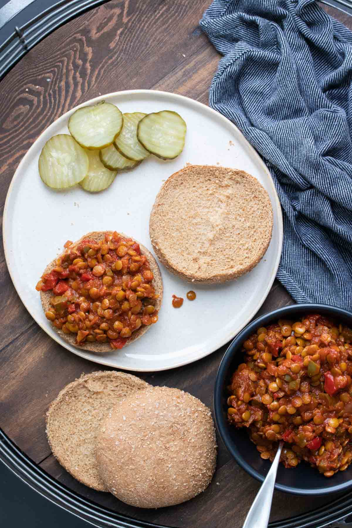 Open faced lentil based sloppy joe on a white plate with pickles on the side