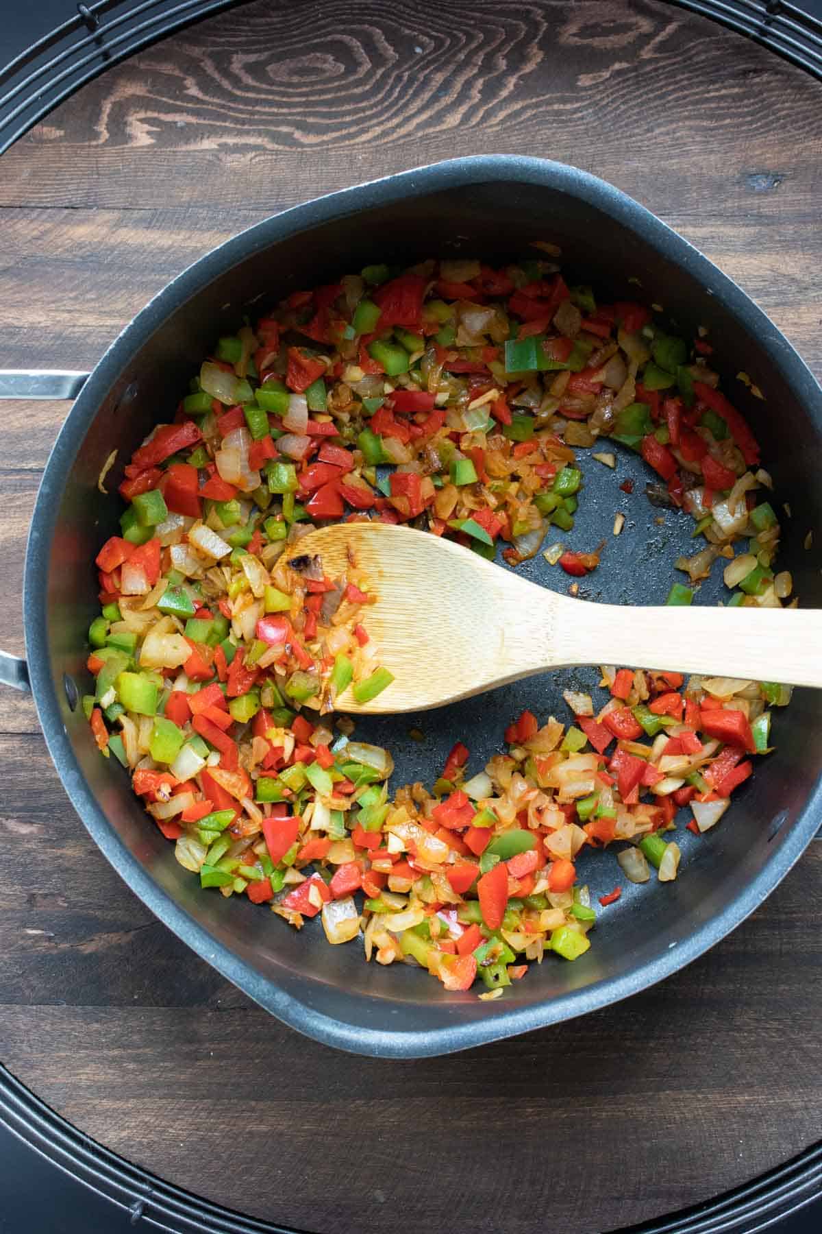 Wooden spoon sauteing peppers and onions in a pan.