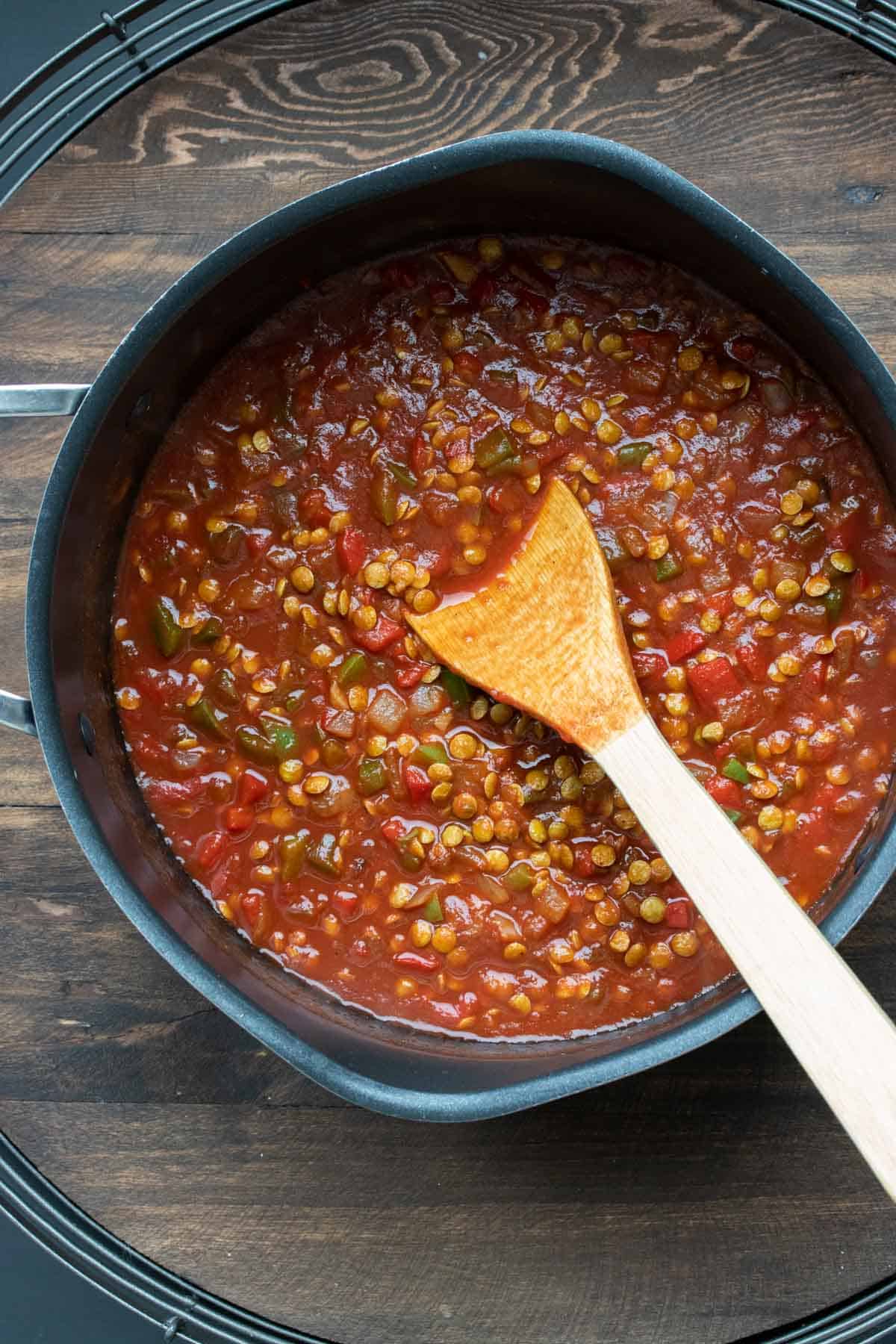 Tomato broth base with lentils and veggies being stirred in a pan.