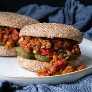 A bun with sloppy joes inside of it sitting on a white plate.