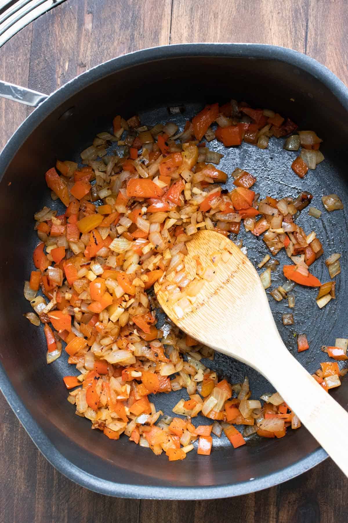 Wooden spoon mixing peppers and onions as they cook in a pot.