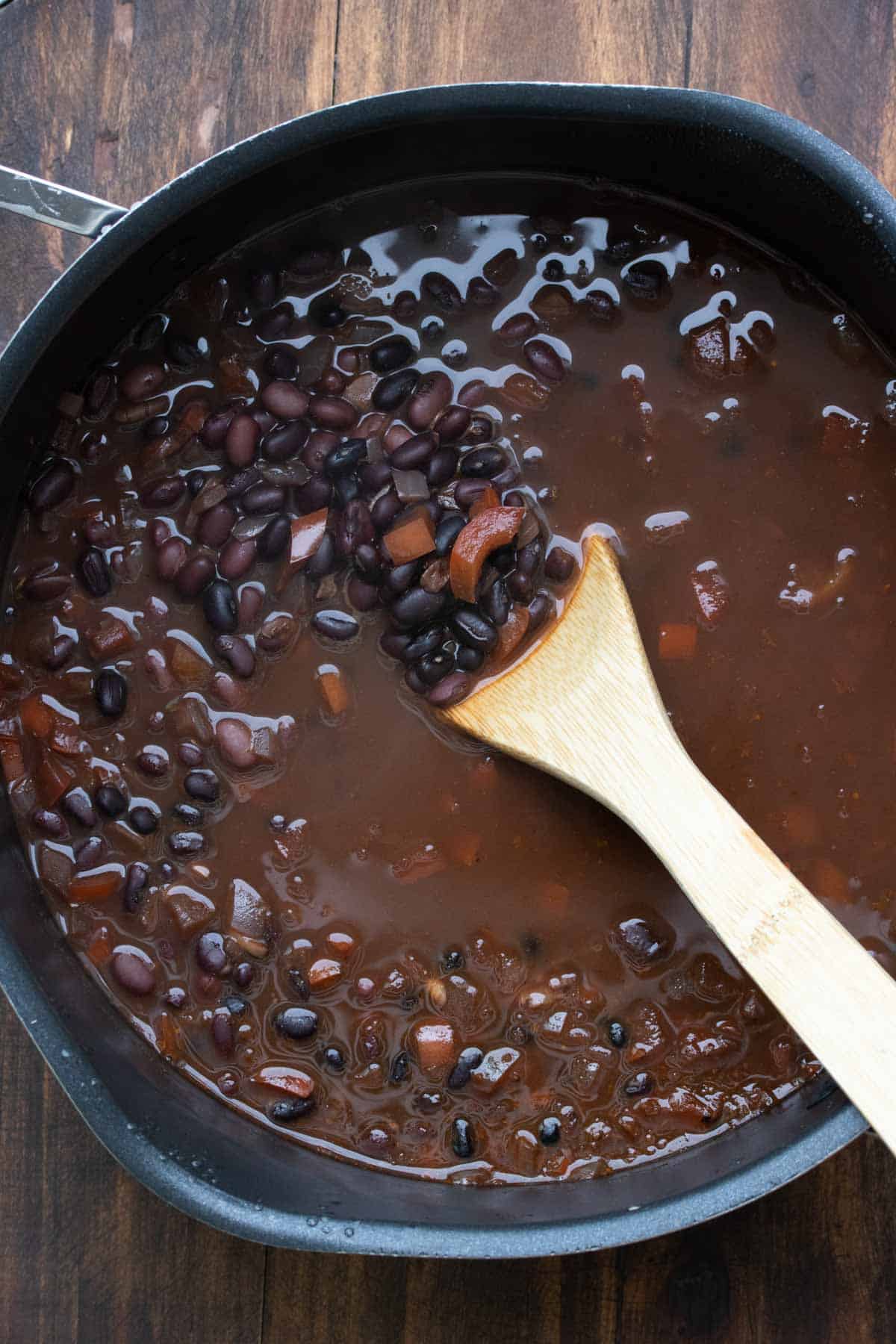 Black beans and chopped peppers in broth being mixed in a pot.