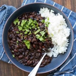 A blue bowl on a blue striped towel that is filled with black beans and white rice with cilantro on top.