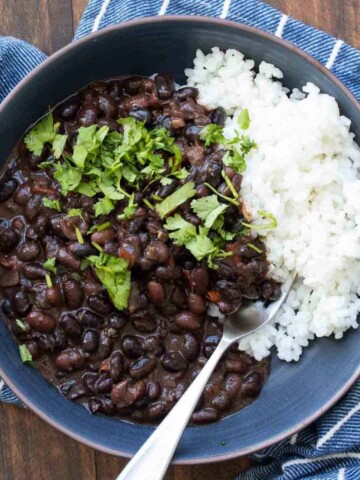 A blue bowl on a blue striped towel that is filled with black beans and white rice with cilantro on top.