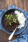 Black beans and white rice topped with chopped cilantro in a blue bowl sitting on a blue striped towel.